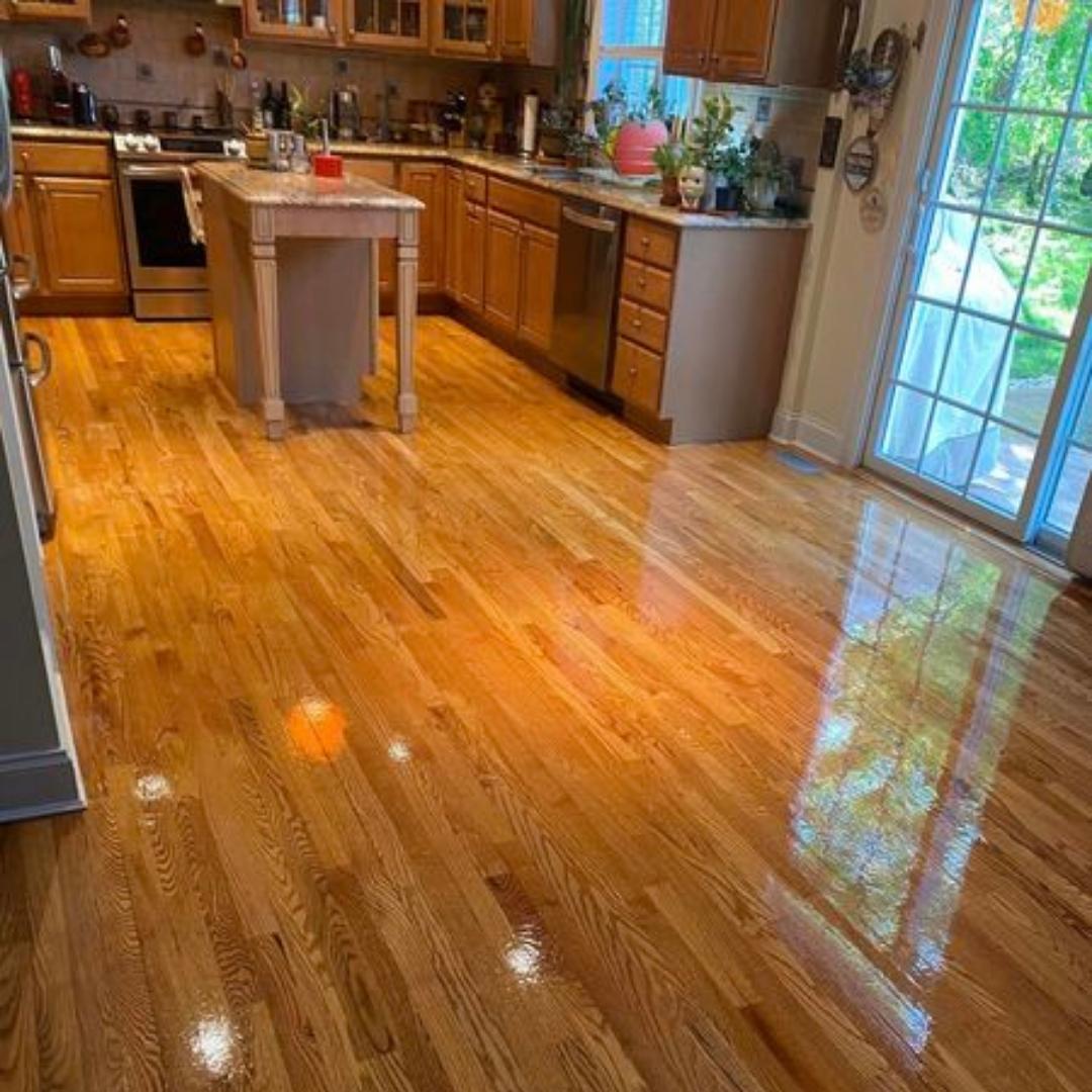 Refinished-hardwood-floor-with-a-glossy-finish-in-a-spacious-living-room-with-green-walls-and-large-windows-providing-natural-light.-1.jpg